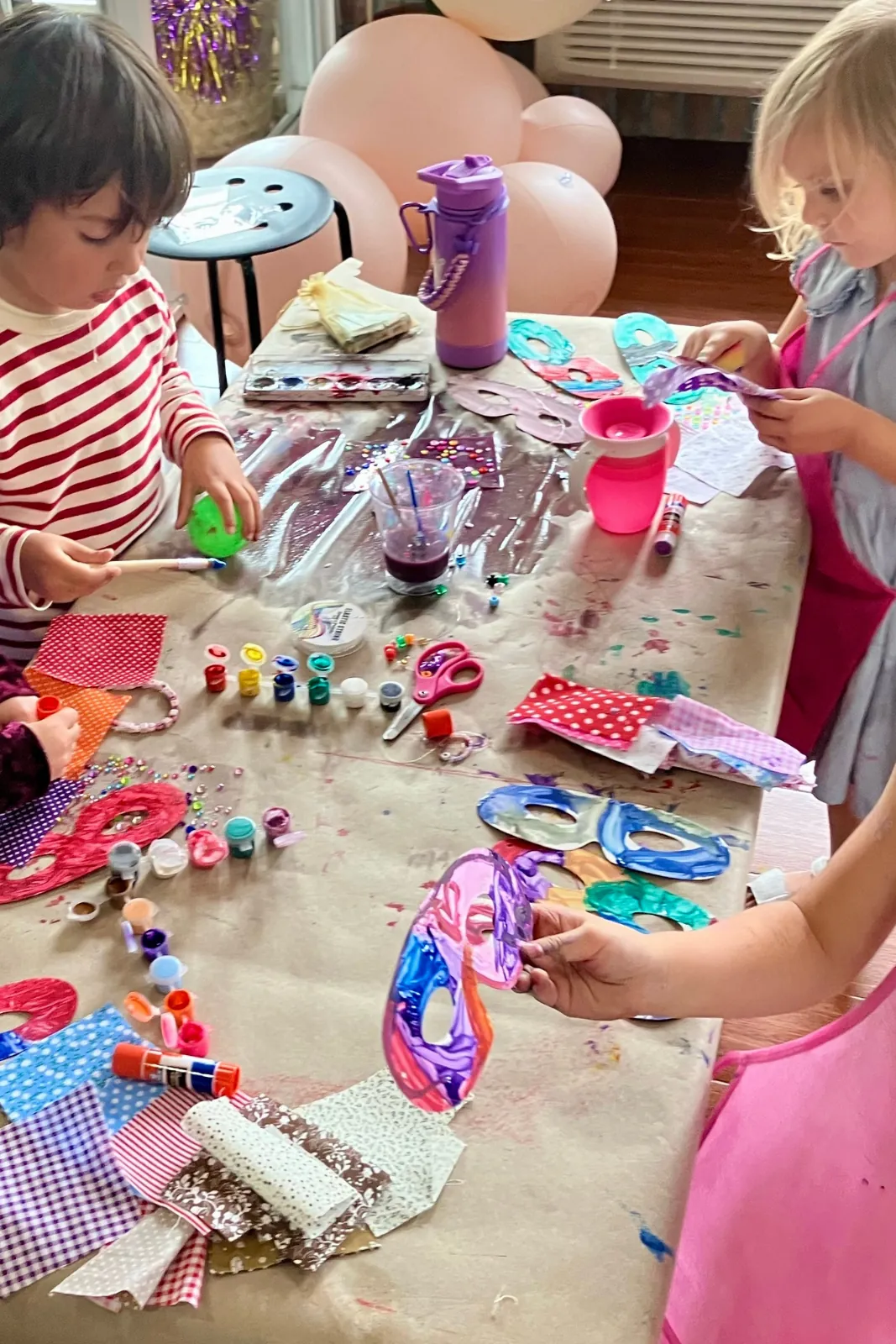 Kids crafting masks and jewelry at a party table