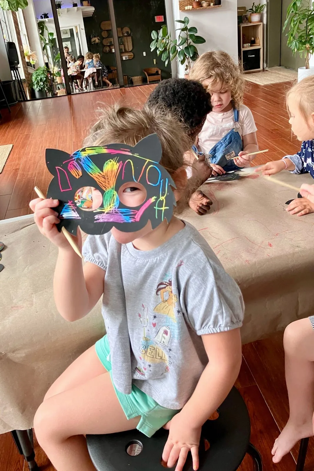 Child wearing a decorated cat mask at the craft table