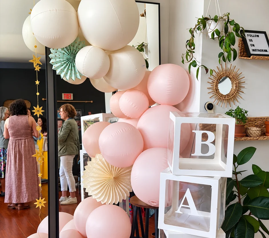 Blush and ivory balloon garland with BABY letter blocks beside a mirror at Green Boutique
